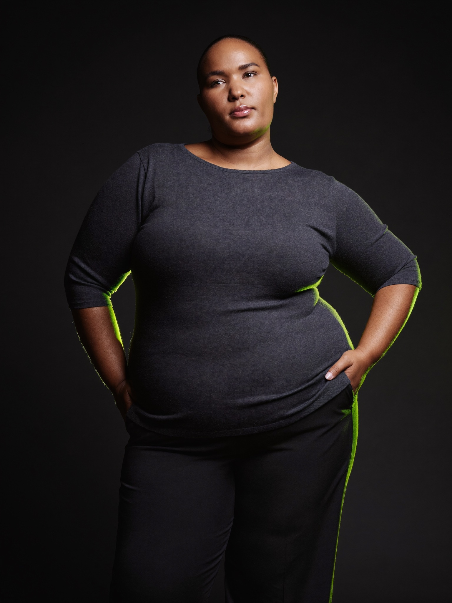 A confident adult standing tall years after a bariatric weight-loss journey, fully clothed, in a matte-black editorial setting